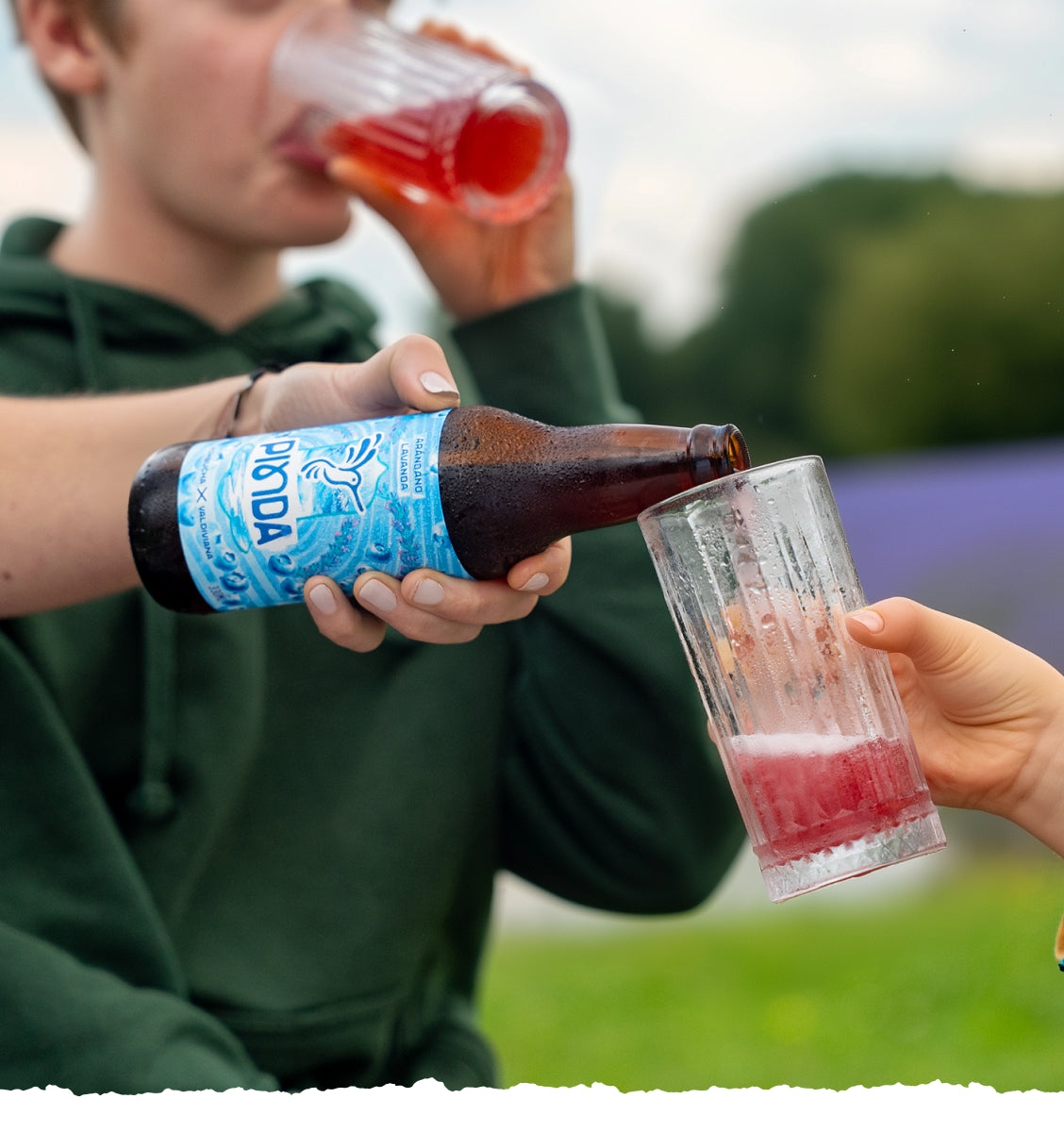Familia comparte kombucha Pinda en naturaleza. Madre sirve bebida viva con fruta real a niños. Ritual de bienestar con super bebida probiótica en campo de lavanda.